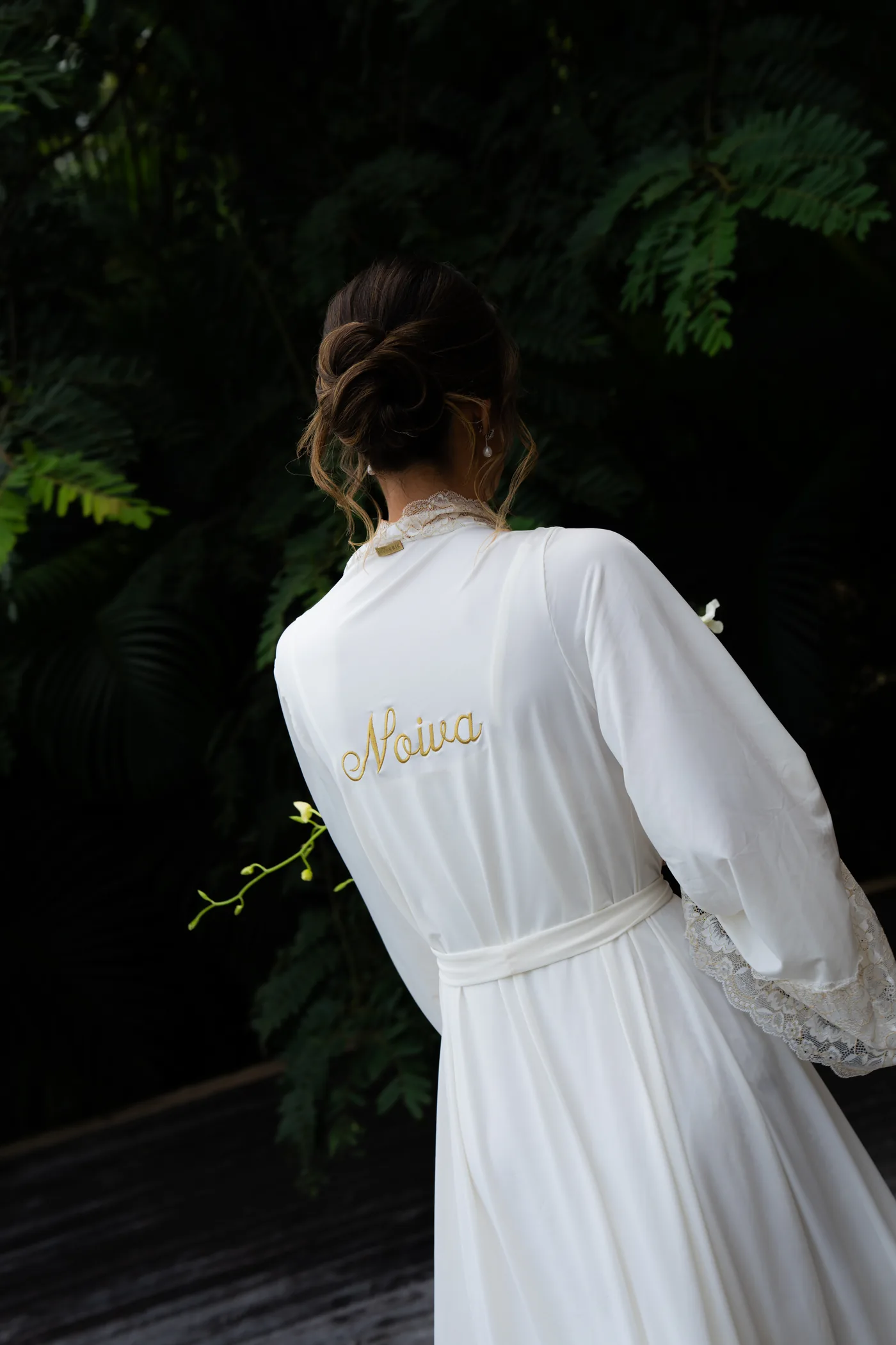 Noiva de costas com o robe bordado, em meio à vegetação