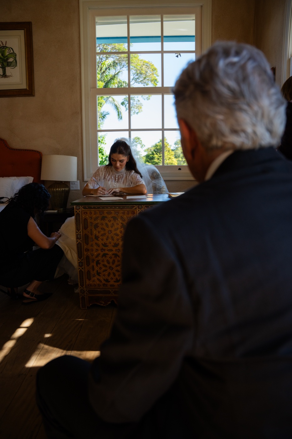 Noiva assinando o registro do casamento, com o pai acompanhando ao fundo, still em preto e branco