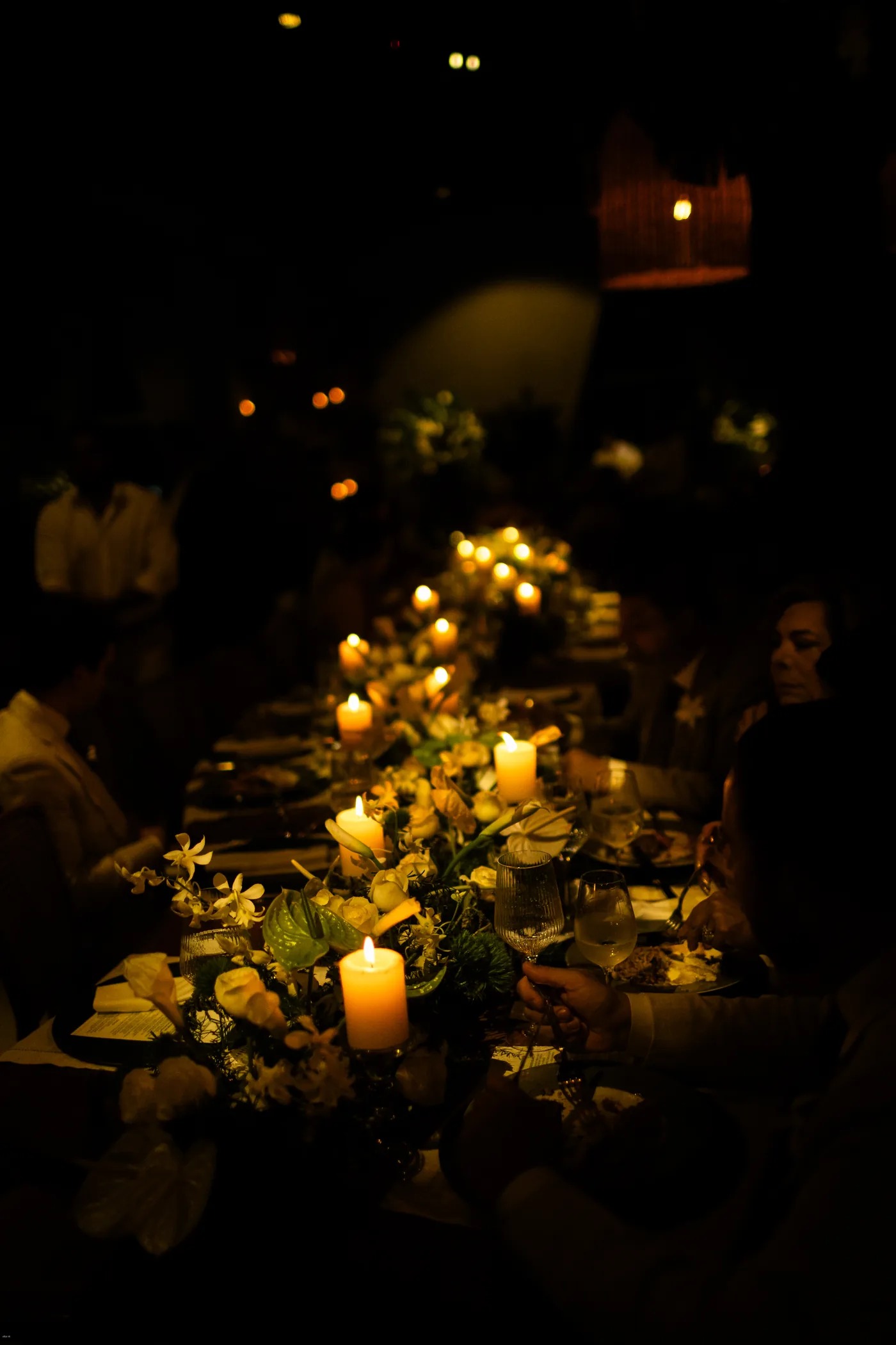 Mesa da festa iluminada por velas, com os convidados sentados